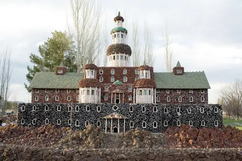 An elaborate stone-built castle structure stands outdoors with a central tower and surrounding trees.
