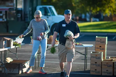 Two people select produce at an outdoor market.