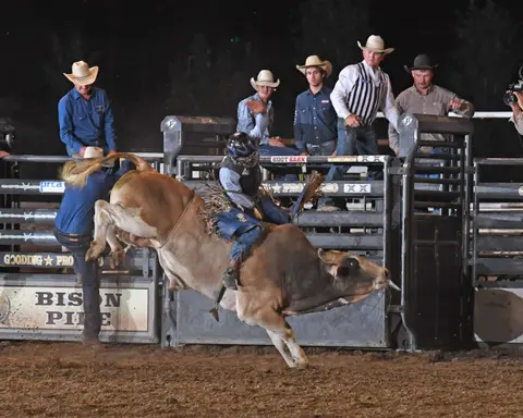 A bull rider on a bucking bull in a rodeo arena.