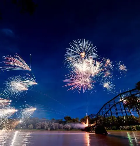 Fireworks light up the night sky over a bridge and water.