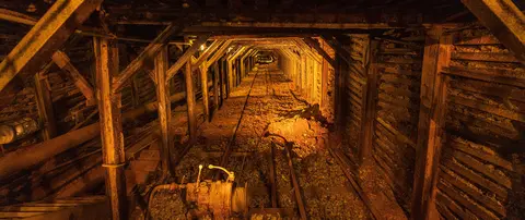 An underground mine tunnel supported by wooden beams with tracks running through it.
