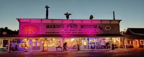 An exterior view of a building with a large sign illuminated by pink lights at dusk.