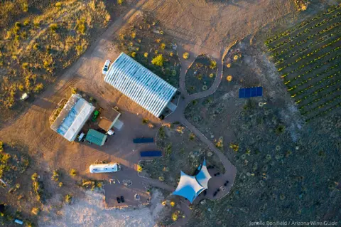 An aerial view shows a rural property with buildings, a greenhouse, and a vineyard.