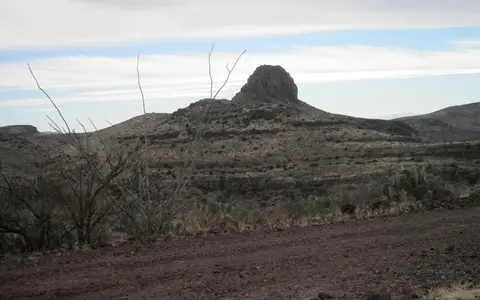 A rocky desert landscape with a prominent hill under a cloudy sky.