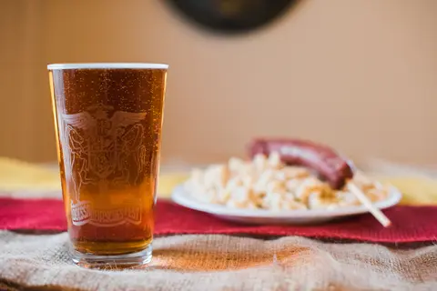 A glass of beer and a plate of food sit on a table.