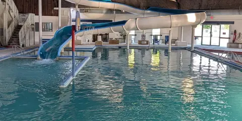 An indoor swimming pool with a water slide and basketball hoop.