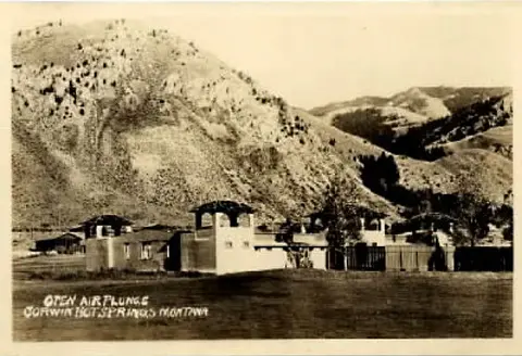 Historic sepia photo showing a building below a large hill or mountain.