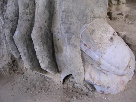 A stone sculpture of massive fingers crushing a car into the ground.