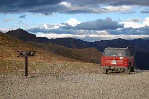 A red vehicle parked on a mountain pass next to a sign.