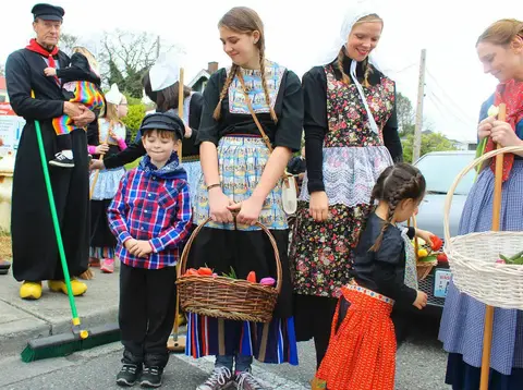 People dressed in traditional Dutch attire hold baskets and stand outside.