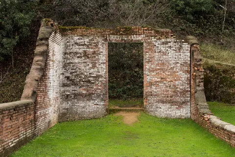 A ruined brick structure with a central doorway stands outdoors.