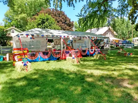 A decorated outdoor tent with patriotic bunting and hay bales set up on a grassy lawn.