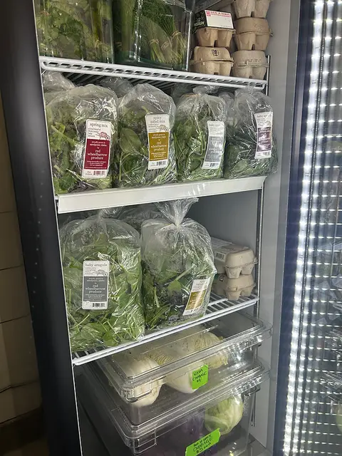 A refrigerated display case filled with fresh produce, herbs, and eggs.