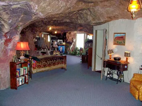 An interior view of a room carved into rock with a bed and furniture.