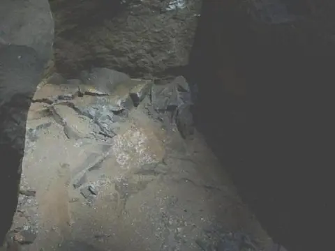 A dark rocky cavern with a sandy floor.