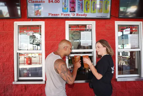 A man and a woman pick up drinks at a service window.