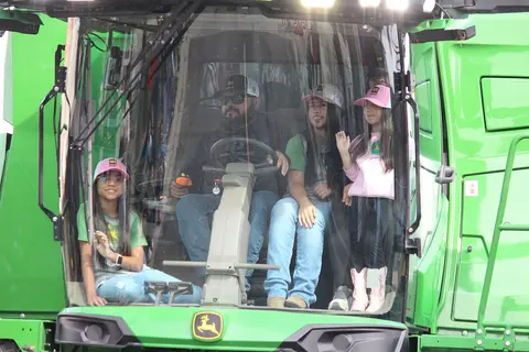 Several people sit inside the cab of a large green tractor.