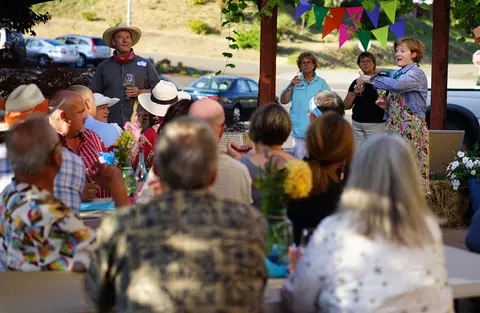 A group of people gather for an outdoor event with tables and colorful banners.