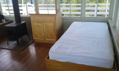 An interior shot of a room with a bed, a wooden cabinet, and a wood-burning stove.