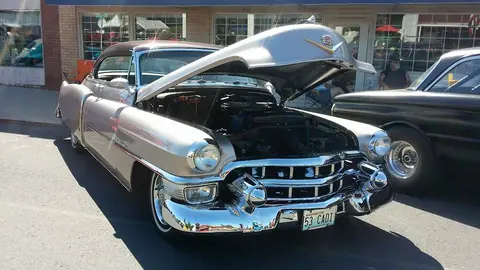 A classic vintage car with its hood open parked on a street.