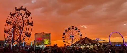 A photograph of carnival rides and a crowd under a bright orange sunset sky.