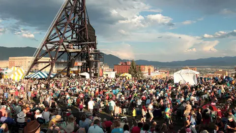 A large crowd gathers for an outdoor event near a tall industrial structure.