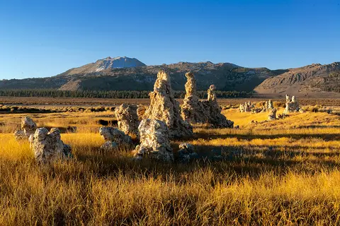 A landscape showing tufa towers in a grassy field with mountains in the background under a clear blue sky.