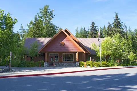 Exterior view of a wooden building surrounded by trees under a clear blue sky.