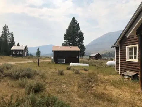 A rural landscape with several wooden cabins and mountains in the background.