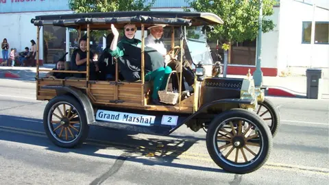 People ride in an antique car during a parade.