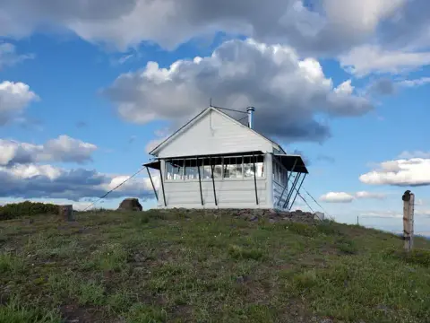 A white lookout building sits on a grassy hill under a cloudy blue sky.