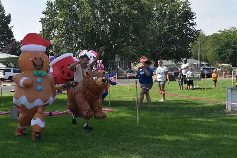 People in inflatable costumes walk across a grassy field during an event.