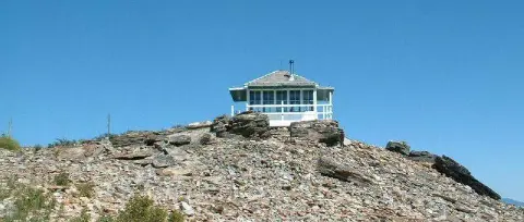 A small white lookout building sits atop a rocky hill against a clear blue sky.