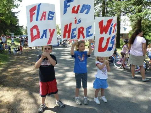 Three children hold up homemade signs at an outdoor event.