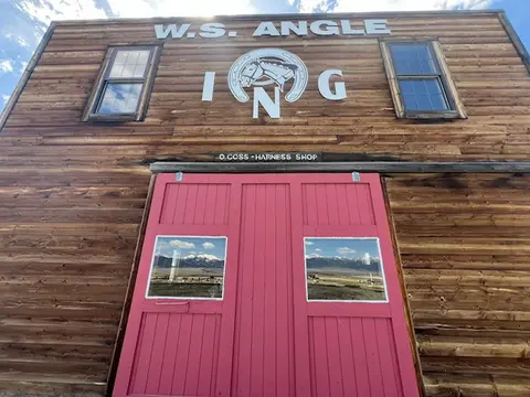 A wooden building exterior features red double doors and lettering on the facade.
