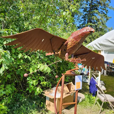 A metal bird sculpture stands outside with wings spread.
