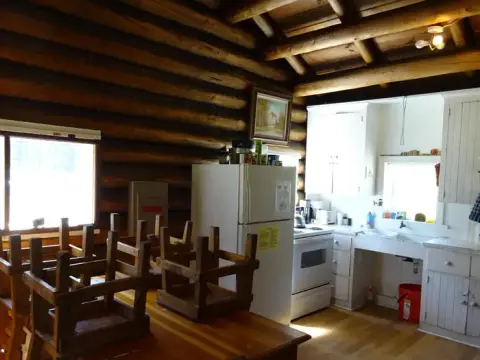 An interior view of a rustic log cabin kitchen with wooden tables and upside-down chairs.