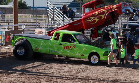 A modified green pickup truck and a red truck with raised body are displayed at an outdoor event.