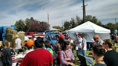 People gather at an outdoor community event with tents and vehicles.