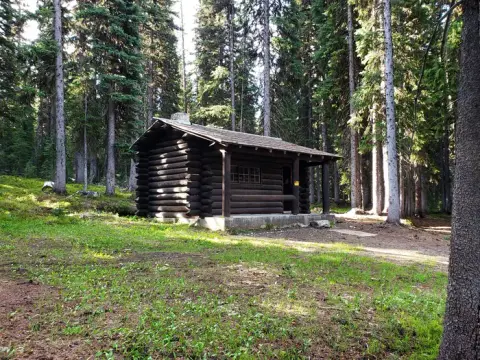 A log cabin sits in a clearing surrounded by tall evergreen trees.