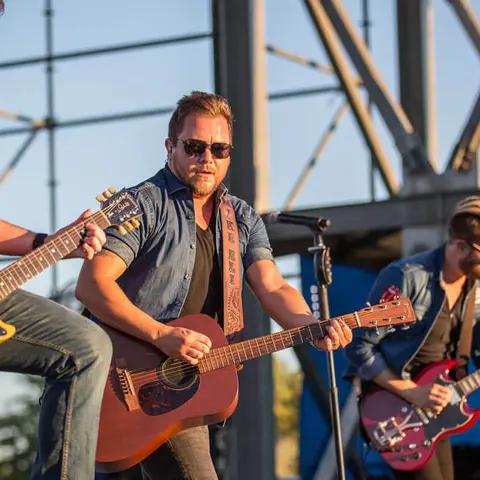 A man plays acoustic guitar on stage with a band.