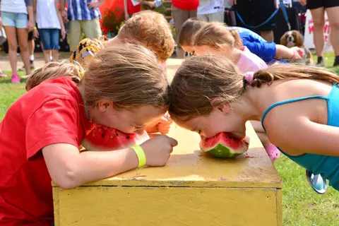 Two children compete in a watermelon eating contest outdoors.