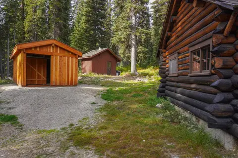 Several wooden cabins stand in a clearing surrounded by a dense forest.