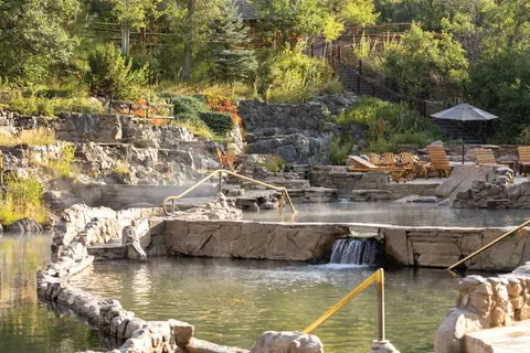 A series of stone hot springs pools are set against a lush hillside with lush greenery.