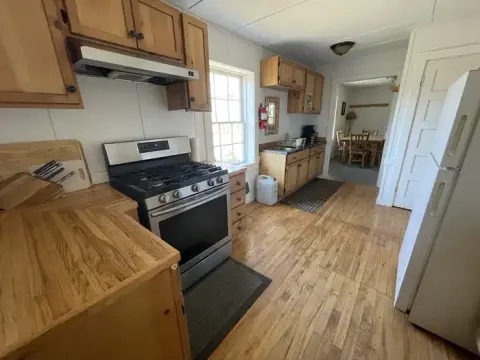 A photo showing the interior of a kitchen with wooden cabinets and flooring.