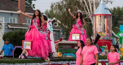 People ride on a parade float decorated in pink and featuring characters.