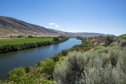A river flows through a wide valley bordered by dry hills and green fields.