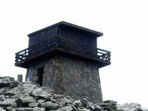 A stone and wooden fire lookout tower stands atop a rocky summit.