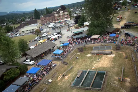 High-angle view of a crowd gathered around an outdoor timber sports venue with a pool and logs.