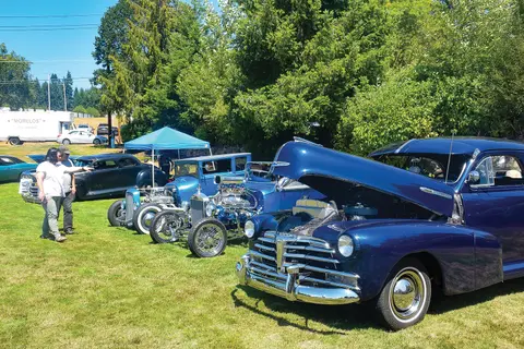 Several classic cars are parked on a grassy field with people looking at them.